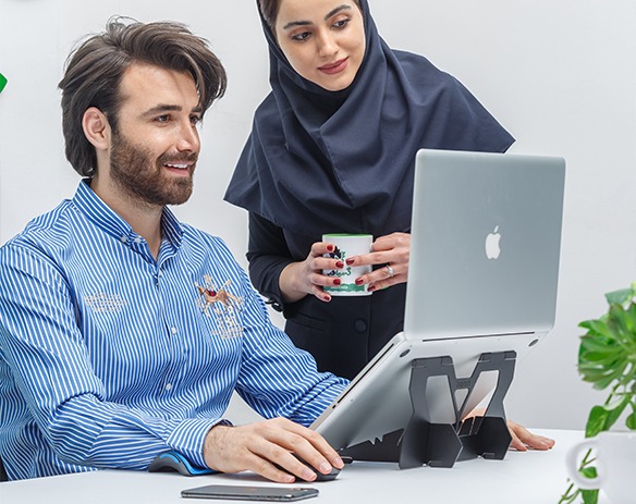 دو همکار یک خانم و یک آقا در حال کار با لپ تاپ هستند که روی زیرلپتاپی قرار دارد.