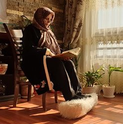 خانم سالمندی روی مبل نشسته است و پاهایش روی روی زیرپایی خز داری گذاشته است